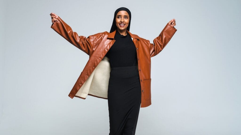 A woman wearing a brown ladies lambskin leather coat with her arms raised, posing confidently