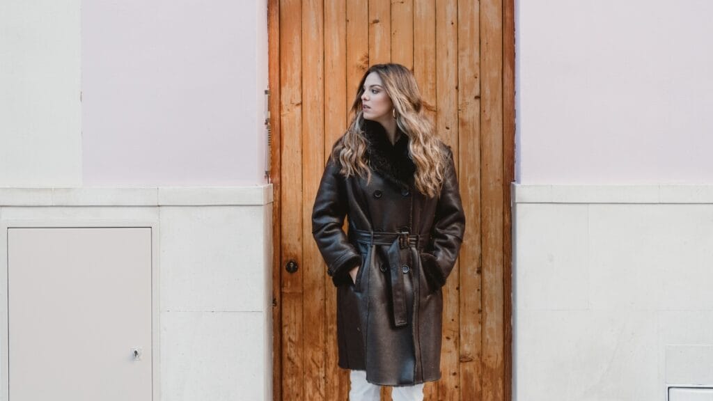 A woman wearing a black ladies lambskin leather coat standing against a wooden wall