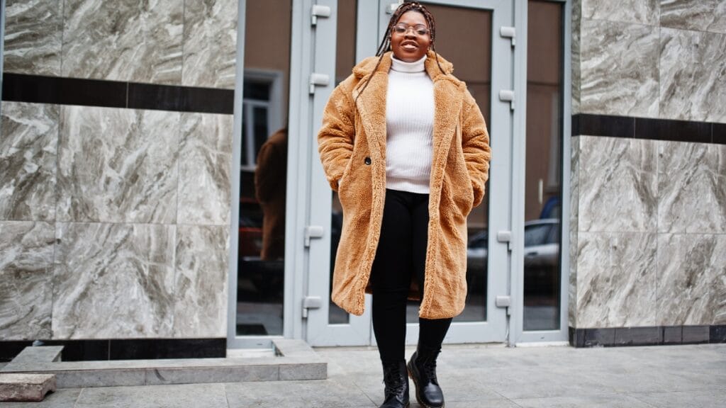 Plus-size woman in a stylish brown winter coat standing in front of a modern building