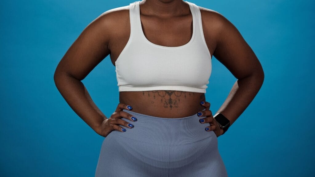 Woman wearing a white sports bra with large cups and light blue leggings, posing against a blue background