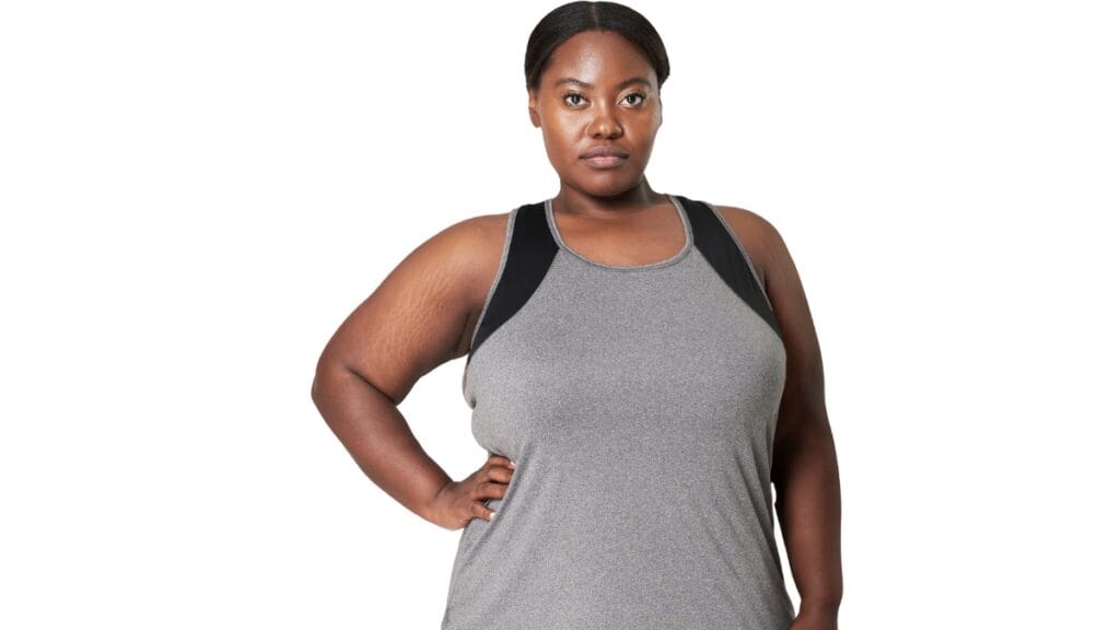 Plus size woman in a gray exercise tank top, standing confidently with hands on hips