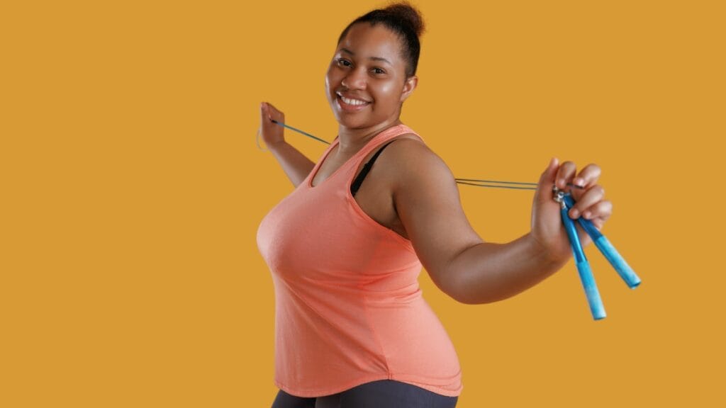 Plus size woman wearing a comfortable orange exercise tank, holding a jump rope with a smile