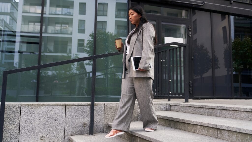 Plus size woman in a grey suit and pants, walking confidently outside with a coffee cup in hand