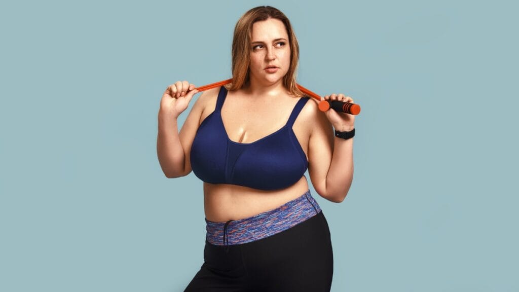 Plus size woman in a blue sports bra and black leggings, holding a resistance band.