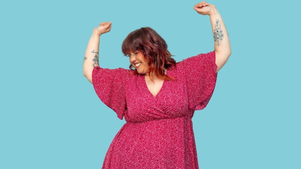 Plus size woman in a pink floral tea dress dancing with arms raised