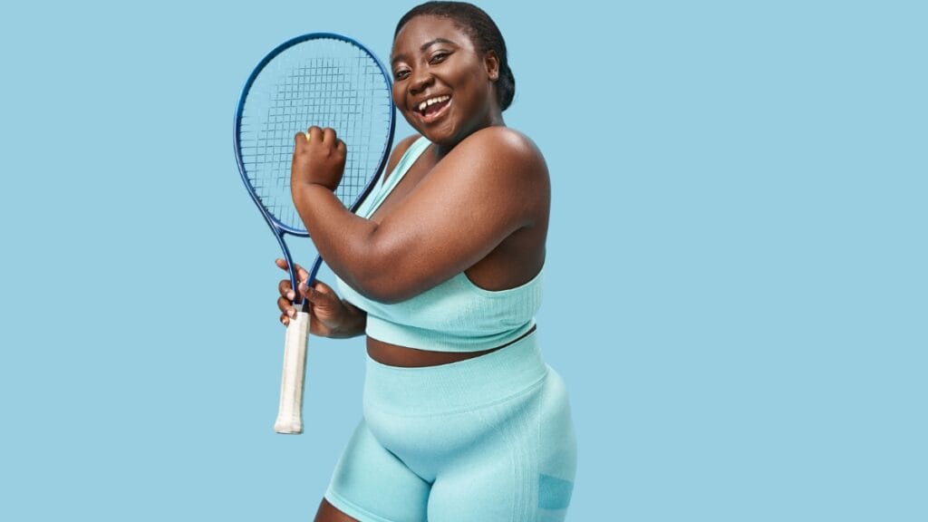 Plus-size woman wearing a tennis outfit and holding a tennis racket, smiling confidently
