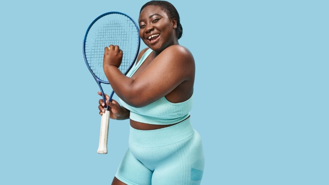 Plus-size woman wearing a tennis outfit and holding a tennis racket, smiling confidently