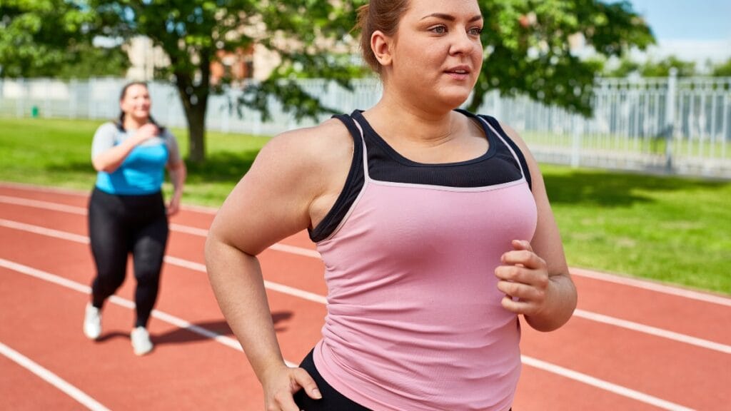 Plus size woman running in a pink workout tank top
