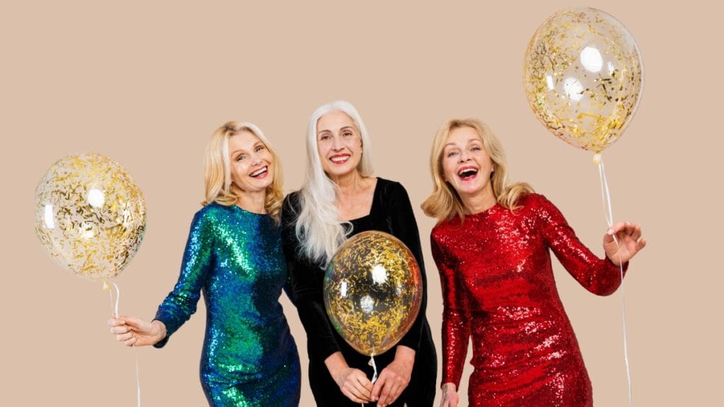 Three women in colorful sequin dresses, holding balloons at a festive event