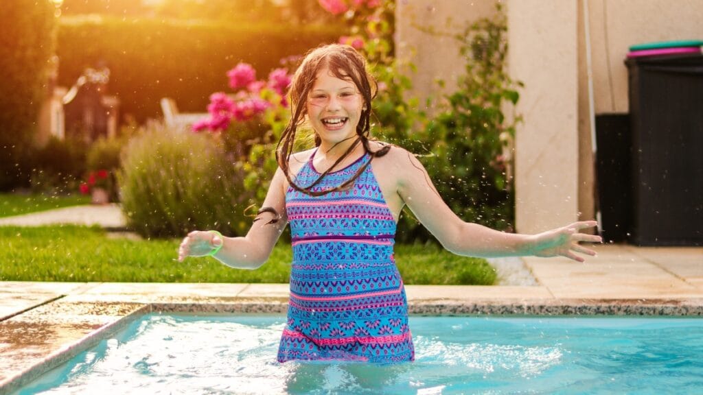 Young girl smiling and playing in a pool while wearing a colorful swim tankini
