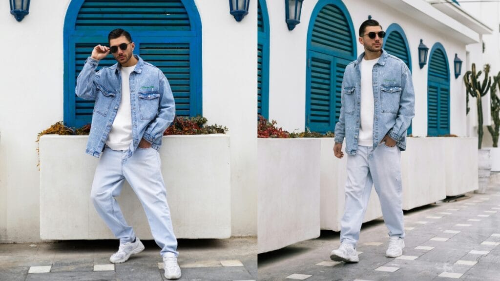 A man wearing a tall denim jacket paired with light denim pants, showcasing a trendy casual look against a vibrant background