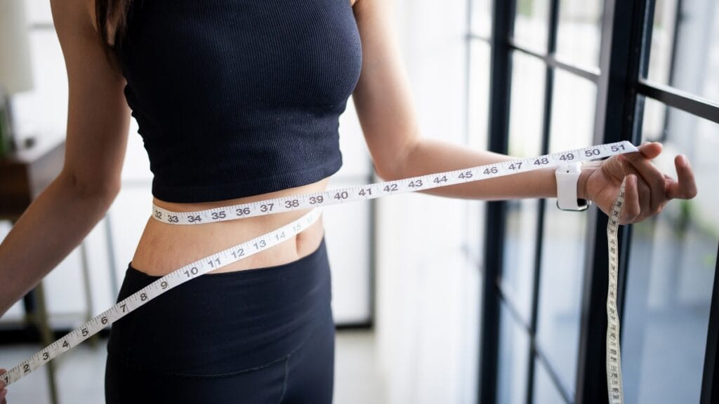 A woman using a measuring tape around her waist for accurate women measurements