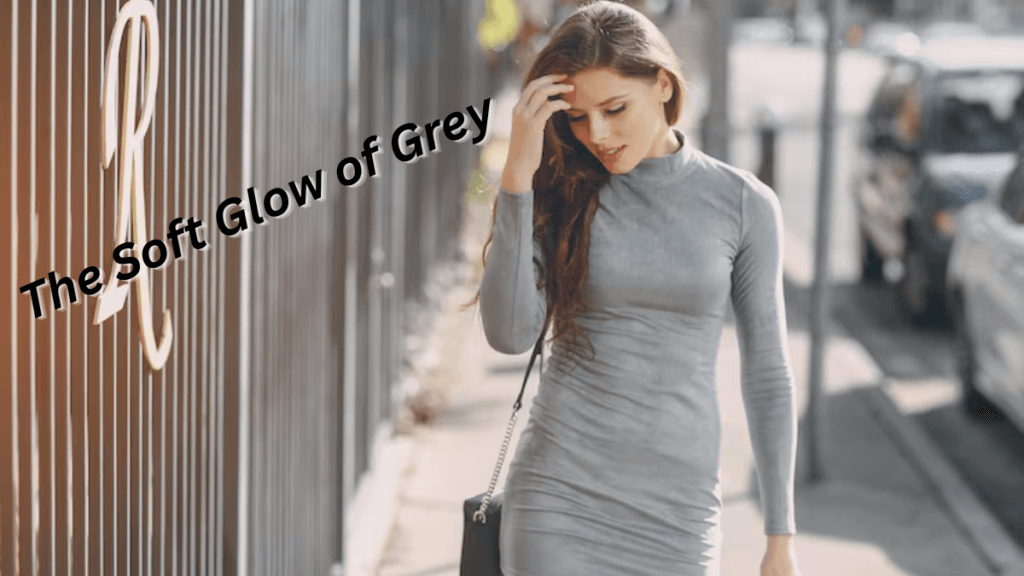 A woman walking on the street in a fitted grey dress, touching her hair while the sun shines in the background.