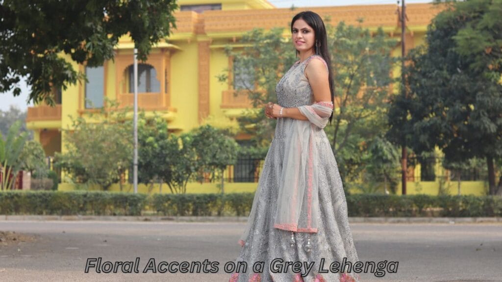 A woman posing outdoors in a grey lehenga with floral accents, complemented by a sheer dupatta and a scenic background.
