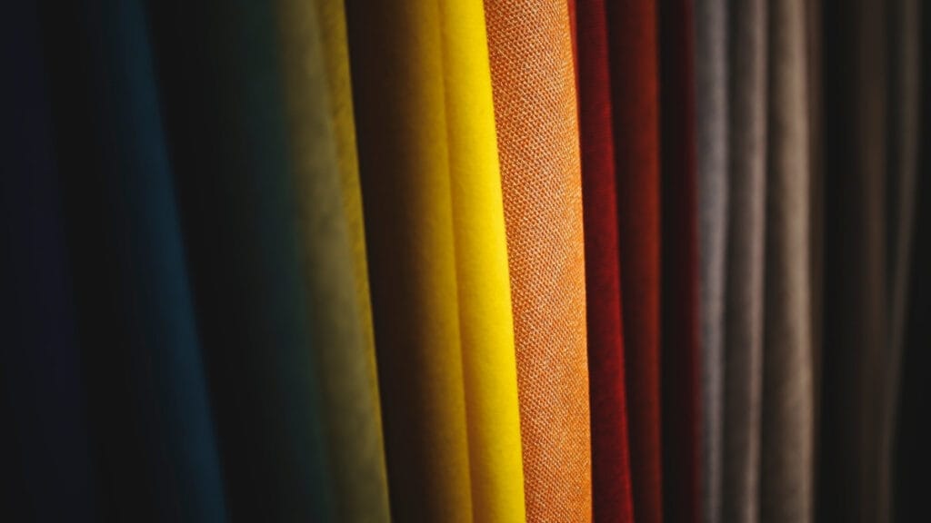 A colorful array of fabrics hanging in a row with various textures and hues, showcasing different fabric properties