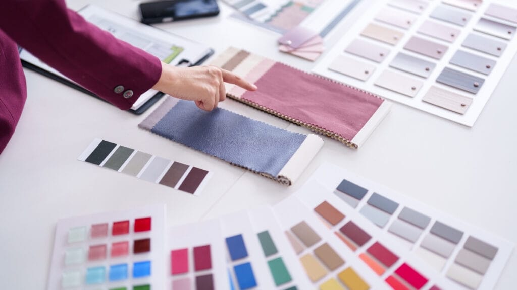 A designer pointing at fabric swatches and color samples laid out on a table, indicating the importance of fabric properties in design