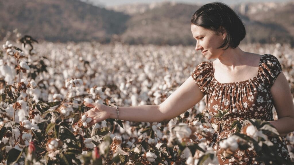 A woman in a floral dress picking cotton in a lush cotton field under a sunny sky