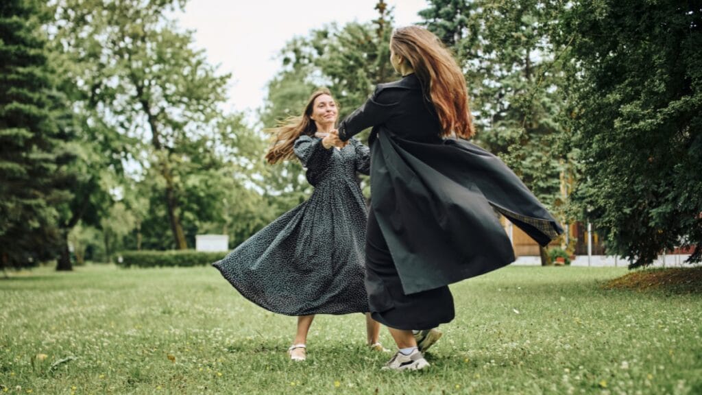 Two women dancing in the park, dressed in flowing dresses, feeling confident with dress spanks for smooth, flattering curves