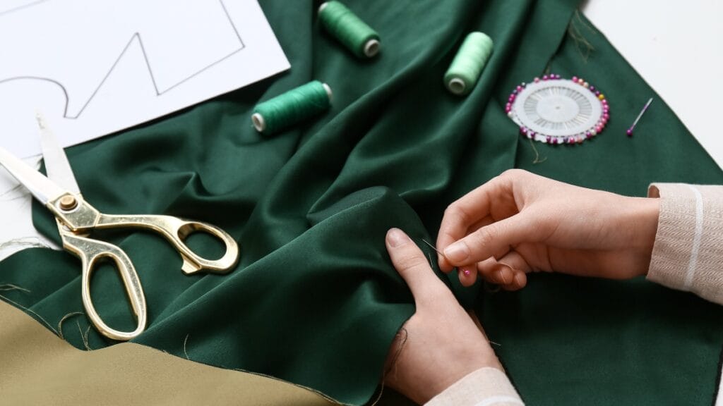 Hand-sewing a green fabric with sewing machine supplies like pins, scissors, and thread