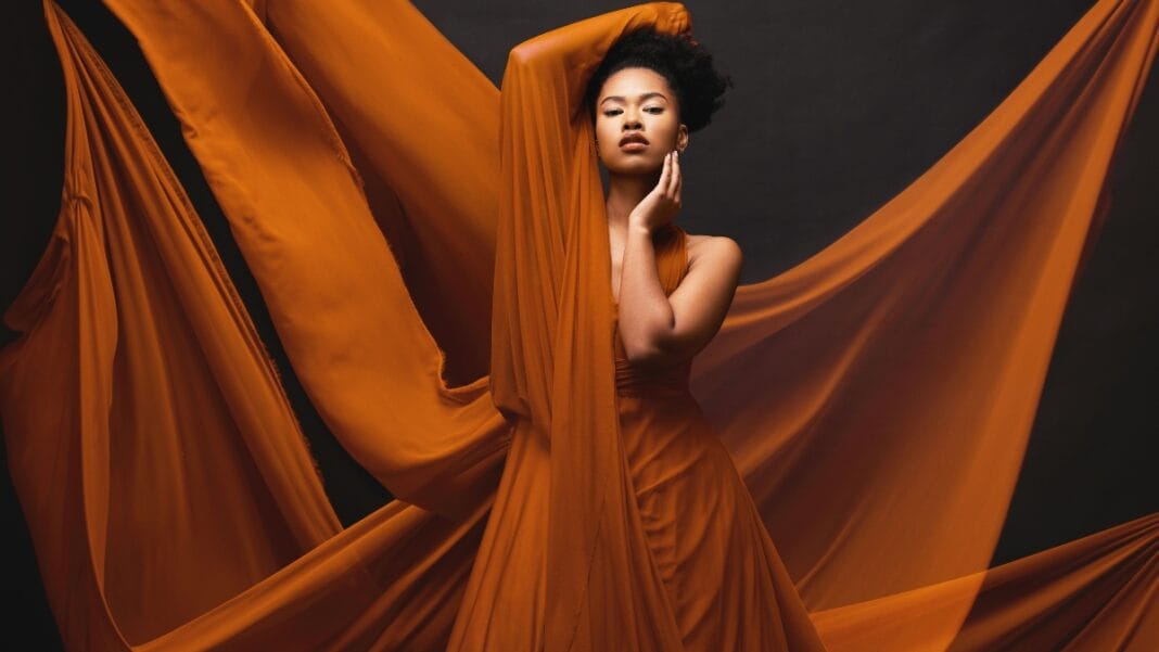 Orange Sheer Fabric Dress – Elegant and Flowing Design Model wearing an orange dress made of sheer fabric, flowing beautifully in a dramatic pose