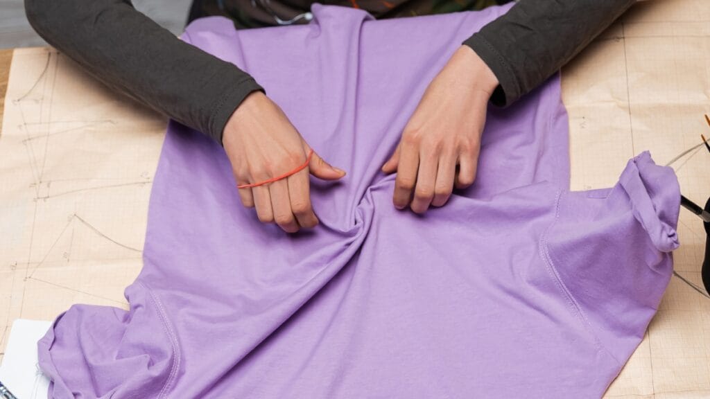 A person stretching a purple shirt made of two-way stretch fabric, demonstrating its flexibility