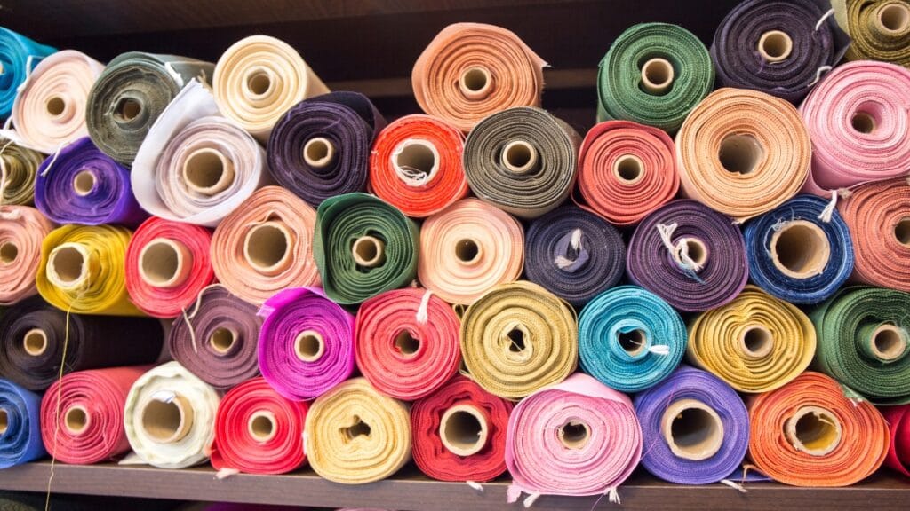 A collection of colorful fabric rolls neatly arranged on a shelf, showcasing various textures and hues, ideal for sewing and design projects