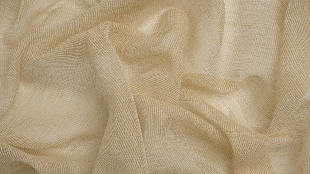 "Close-up of a light, airy sheer fabric draped over a hanger, showcasing delicate translucence and subtle shimmer, with soft natural lighting."