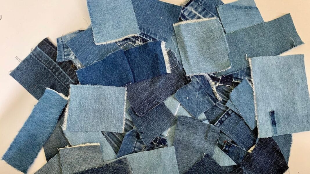 Close-up of unstitched denim fabric with visible diagonal twill weave and indigo dye, highlighting the texture and weight of the fabric.