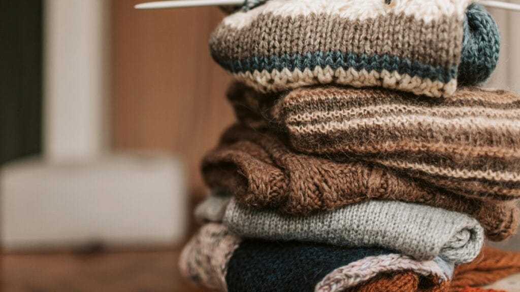 Stack of folded sweaters made from soft knit fabric in neutral colors