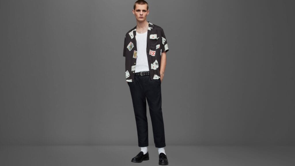 A man in a clothing store examines a bright pink jacket on a clothing rack, with other hanging coats around him and a striped price tag visible.