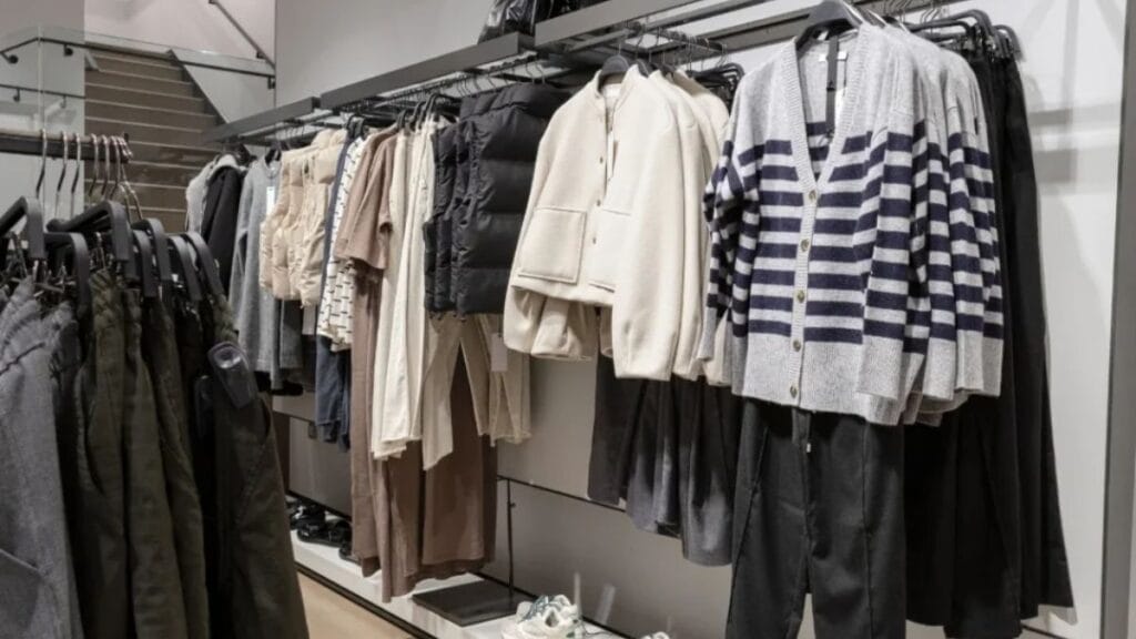 Clothing rack in a retail store displaying neutral-toned sweaters, jackets, and casual apparel neatly arranged on hangers