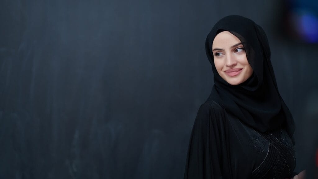 Elegant woman wearing black abaya and hijab set with subtle embellishments against dark background