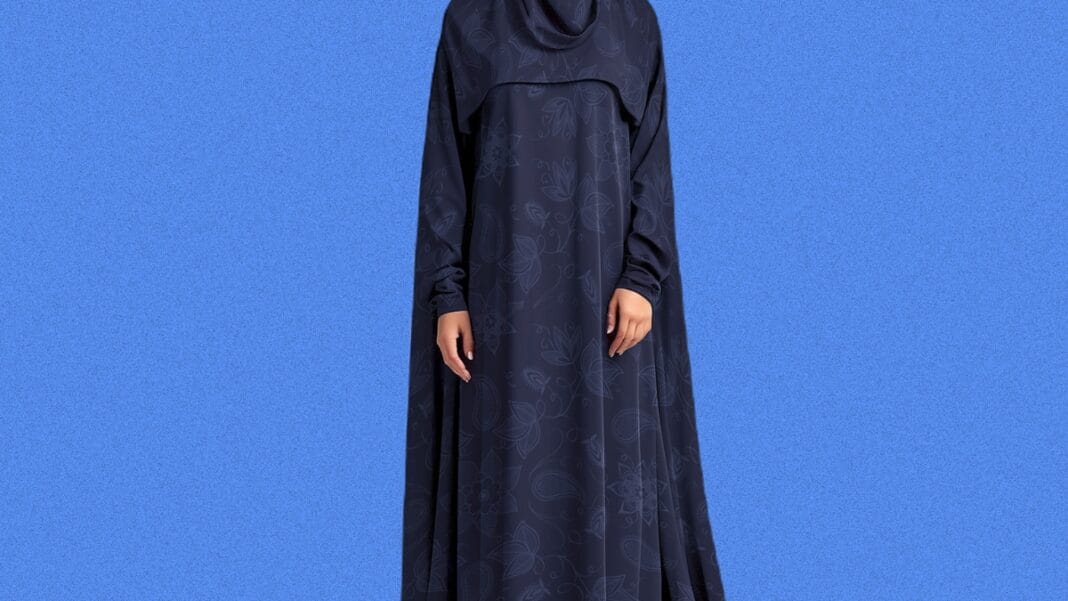 Woman wearing a dark blue abaya against a solid blue background.