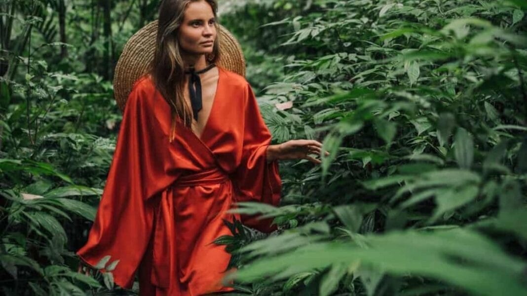 Woman wearing a red viscose dress walking through lush green forest.