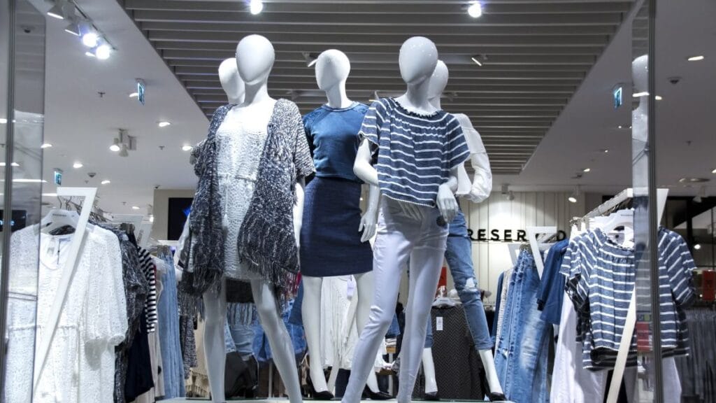 Mannequins displaying casual clothing in a retail store, surrounded by racks of garments under bright indoor lighting.