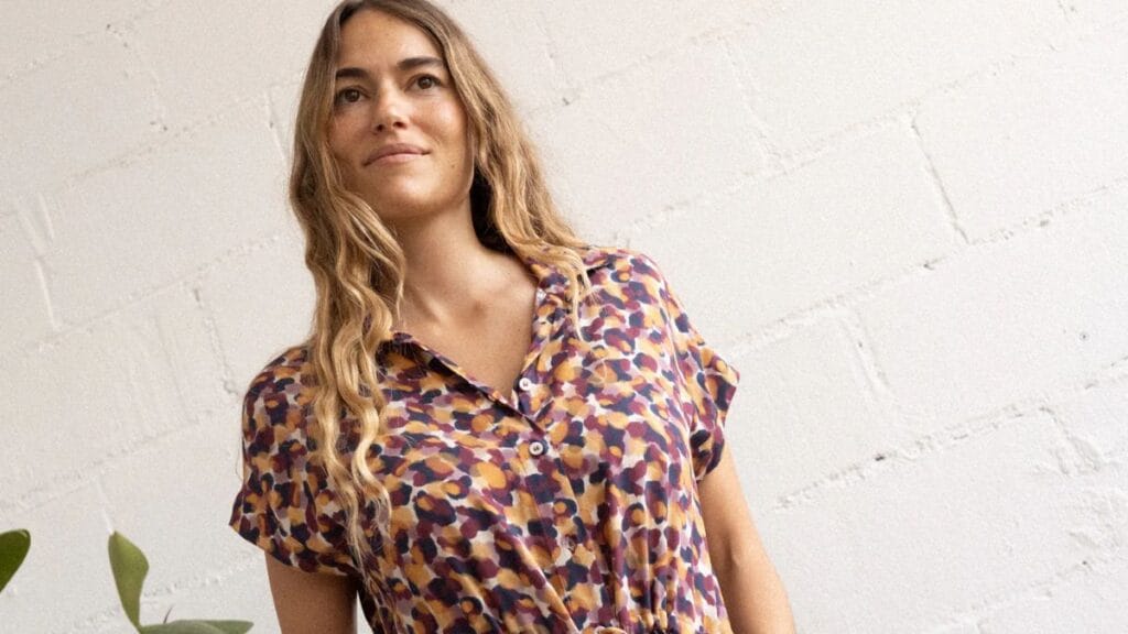 Woman wearing a colorful patterned viscose dress standing against a light textured wall.