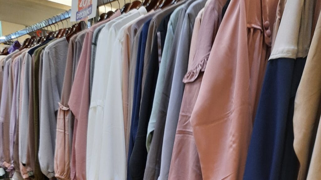 A display of multiple abayas hanging neatly on a rack, showcasing a collection of modest dresses in various colors, fabrics, and styles, arranged side by side for viewing.