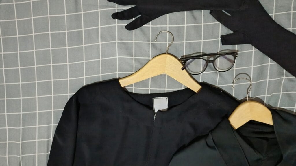 Black abaya set on wooden hanger with matching gloves and accessories displayed on grid background