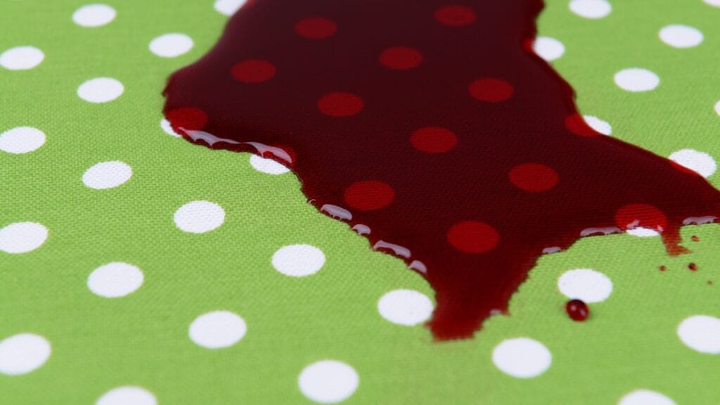 Close-up of a red stain on green fabric with white polka dots—how to get blood out of clothes illustrated on fabric.