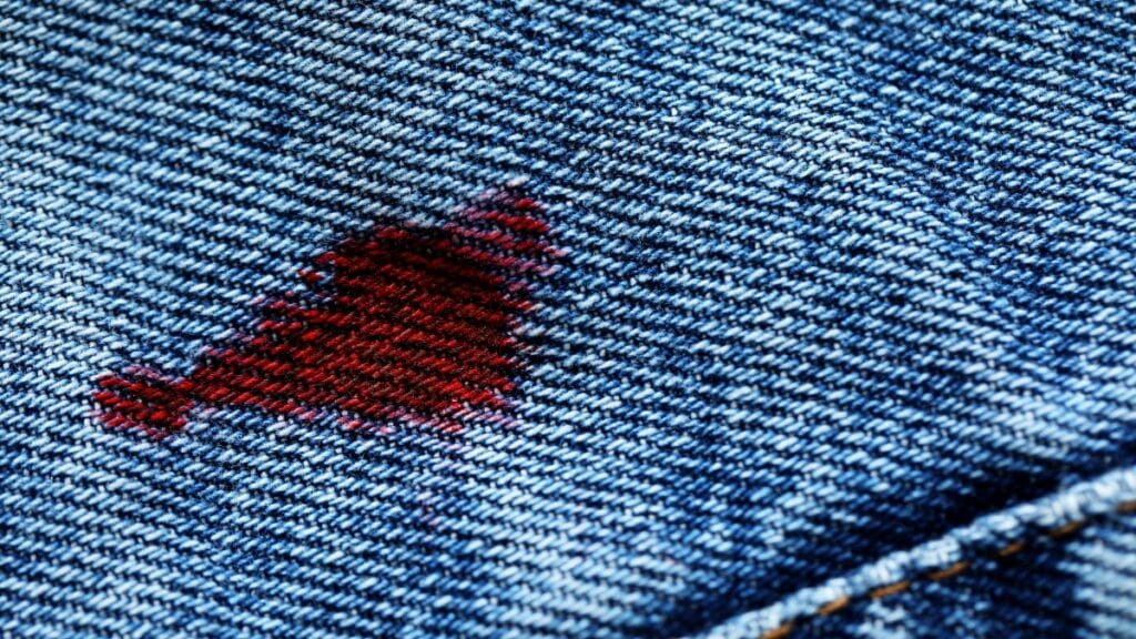 Close-up of a red stain resembling blood on blue denim fabric.