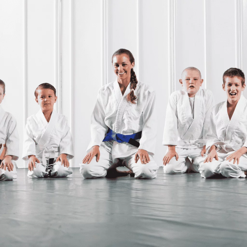 Custom martial arts uniforms by Fashion Soul International featuring a group of martial artists in white karate gis with various belt colors, seated in a traditional dojo.