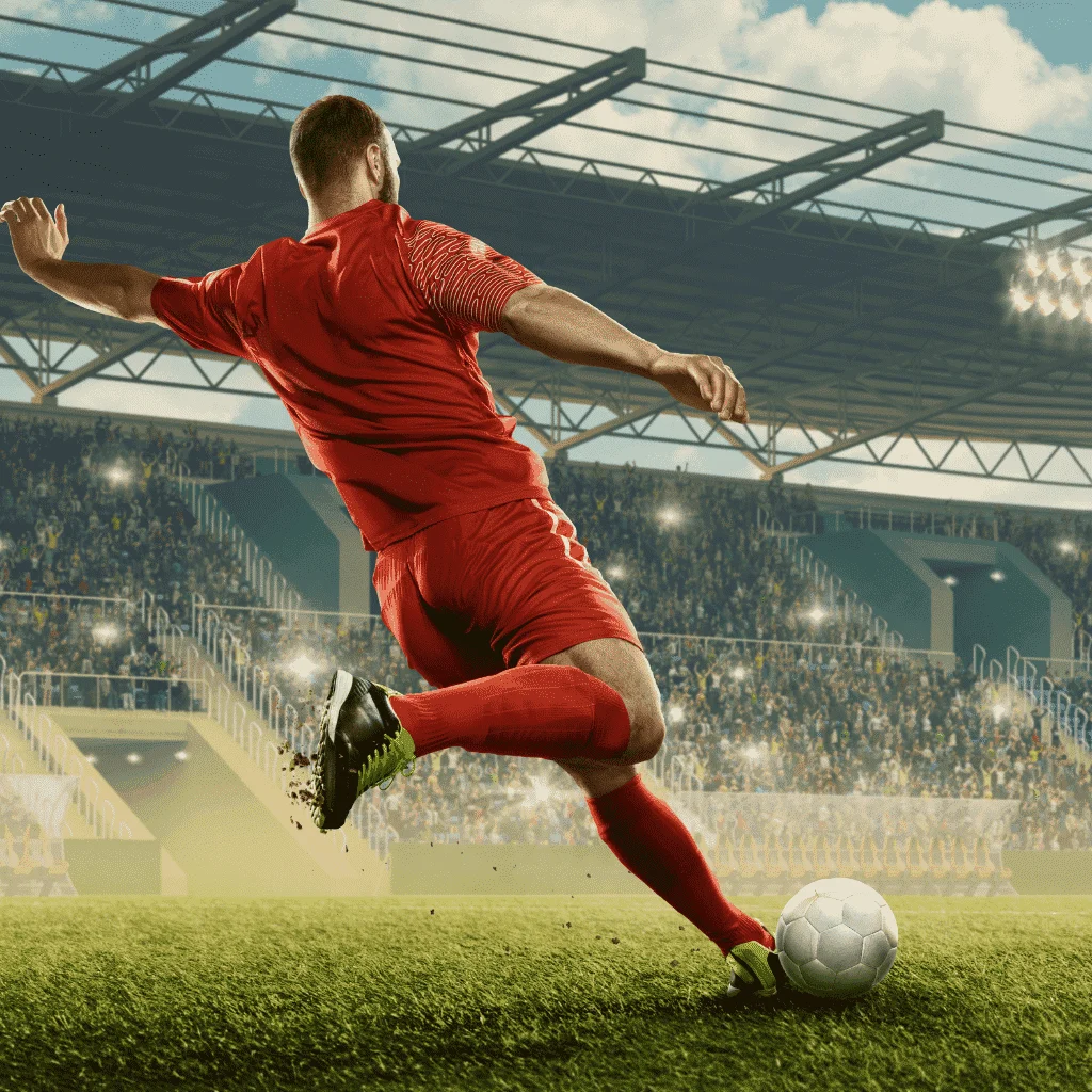 Soccer player in red uniform executing a powerful kick on the field, with a vibrant stadium and enthusiastic crowd in the background.