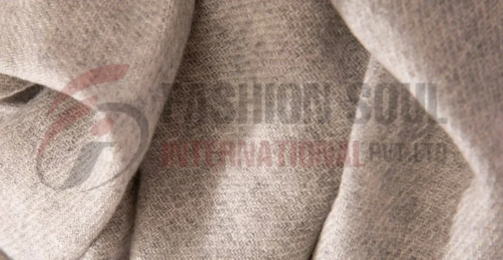 Close-up view of a textured wool fabric in light gray, showcasing a herringbone pattern.