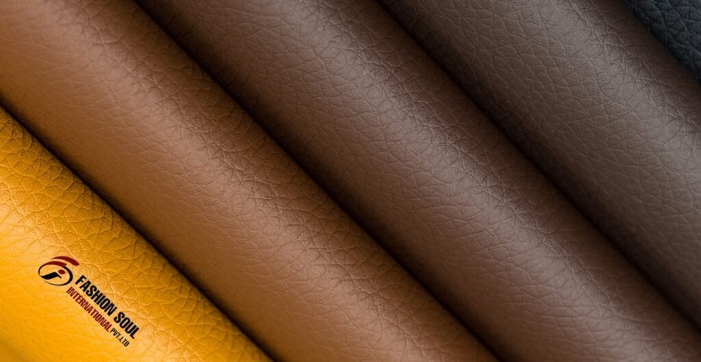 Close-up of four rolls of vegan leather in various shades, including yellow, light brown, dark brown, and black, with a logo in the corner.