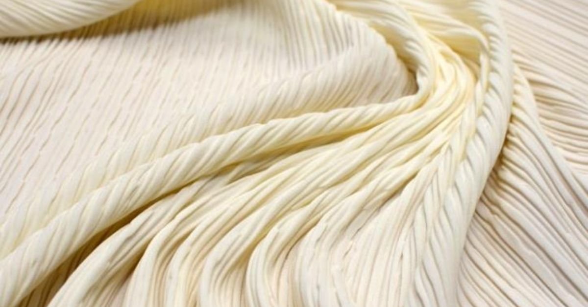 Close-up of cream-colored pleated polyamide fabric with a soft texture and elegant drape.