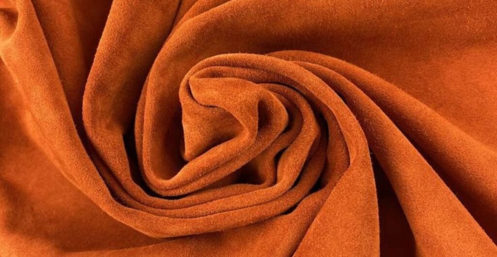 A close-up view of a rolled piece of orange suede leather, showcasing its soft texture and rich color.