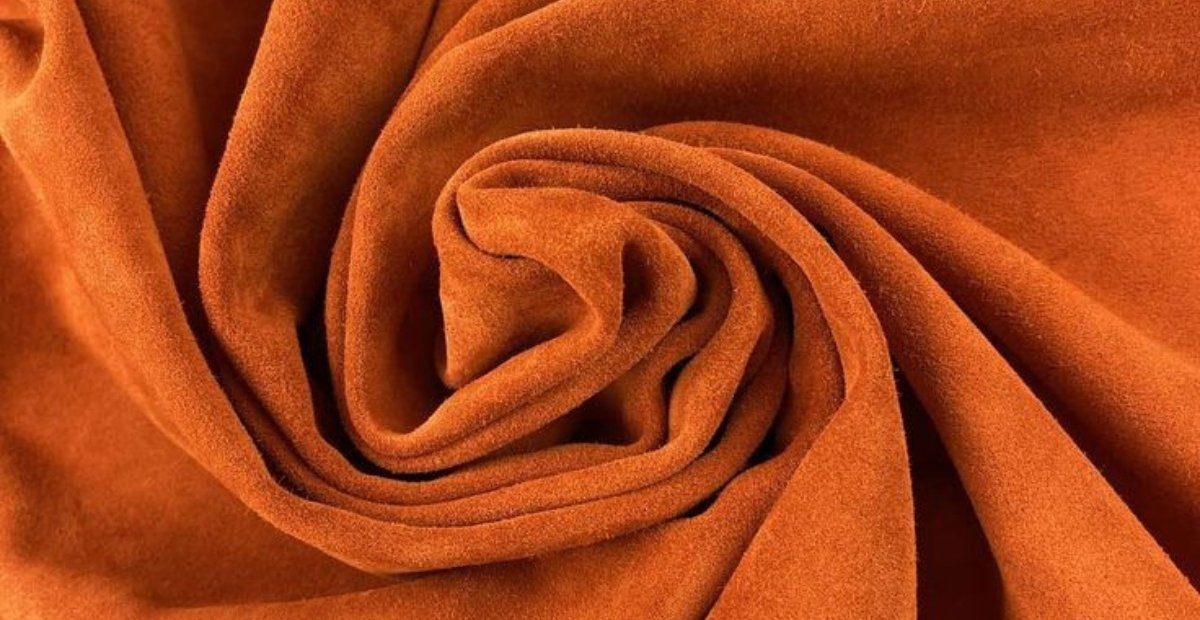 A close-up view of a rolled piece of orange suede leather, showcasing its soft texture and rich color.