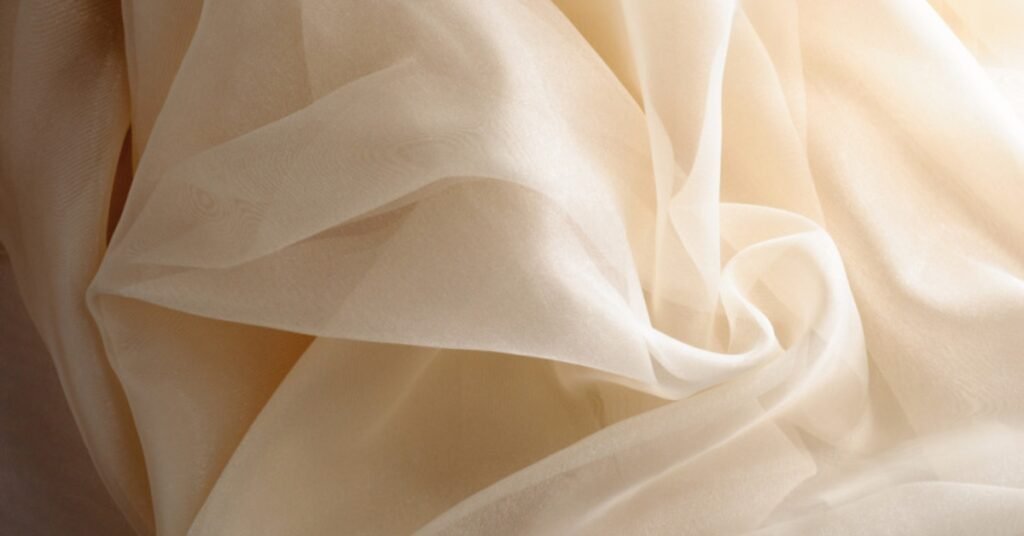 Sheer and lightweight beige organdy fabric with a crisp texture and elegant drape