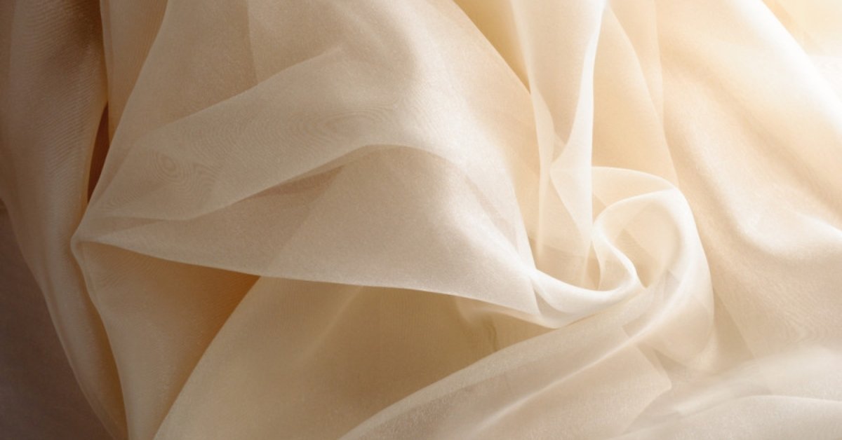 Sheer and lightweight beige organdy fabric with a crisp texture and elegant drape