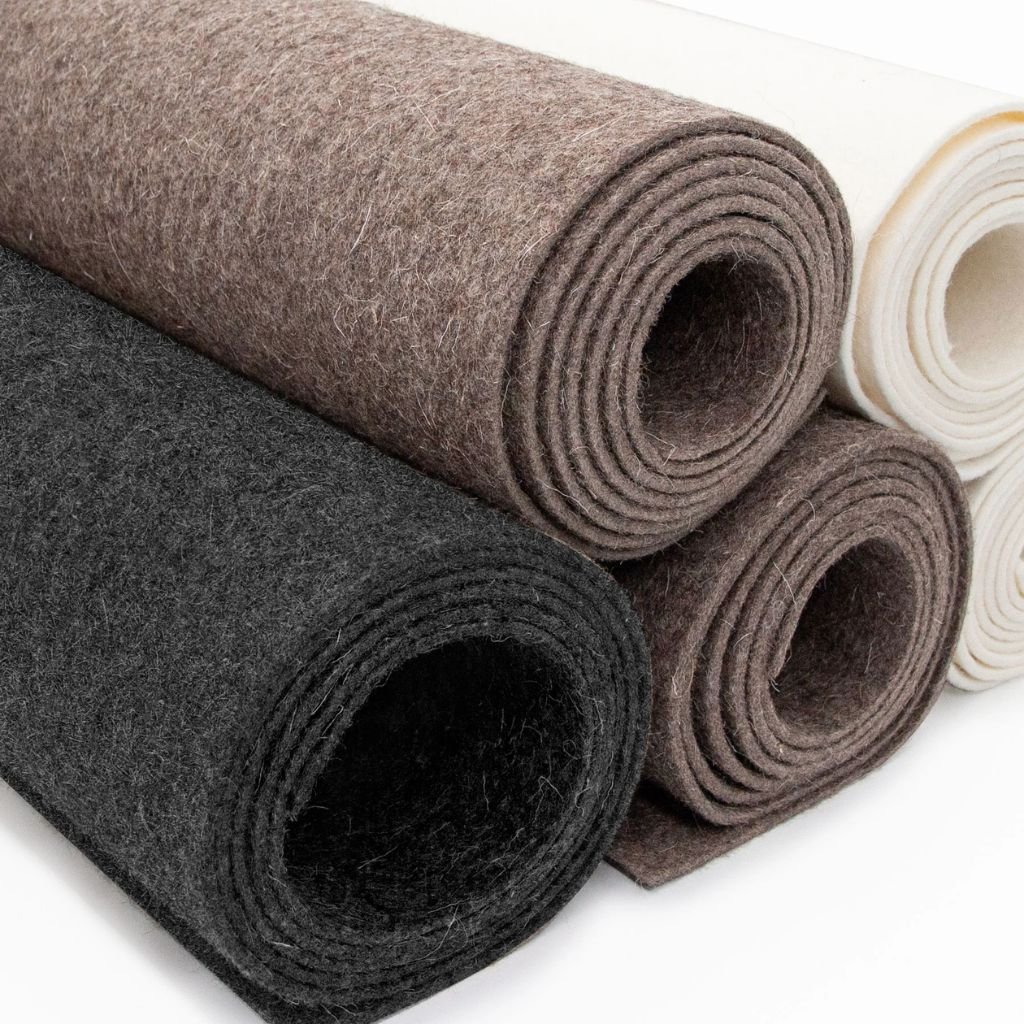 Rolled wool felt fabric in black, brown, and white, showcasing its dense texture and durability.